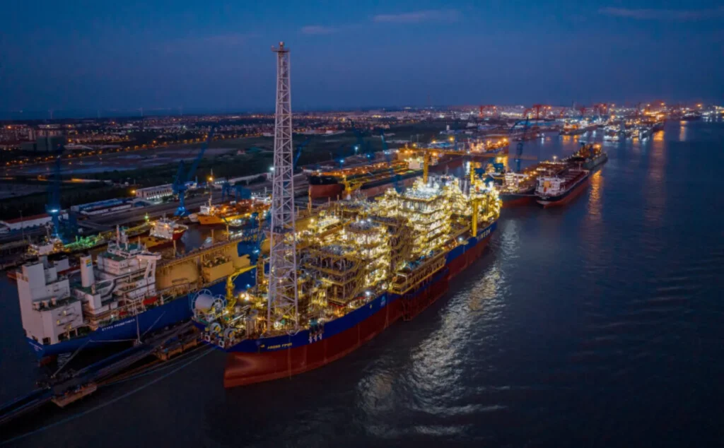 Plataforma flotante FPSO Agogo atracada en un puerto nocturno, rodeada de barcos y con luces brillando en toda su estructura, indicando actividad industrial en el sector energético.